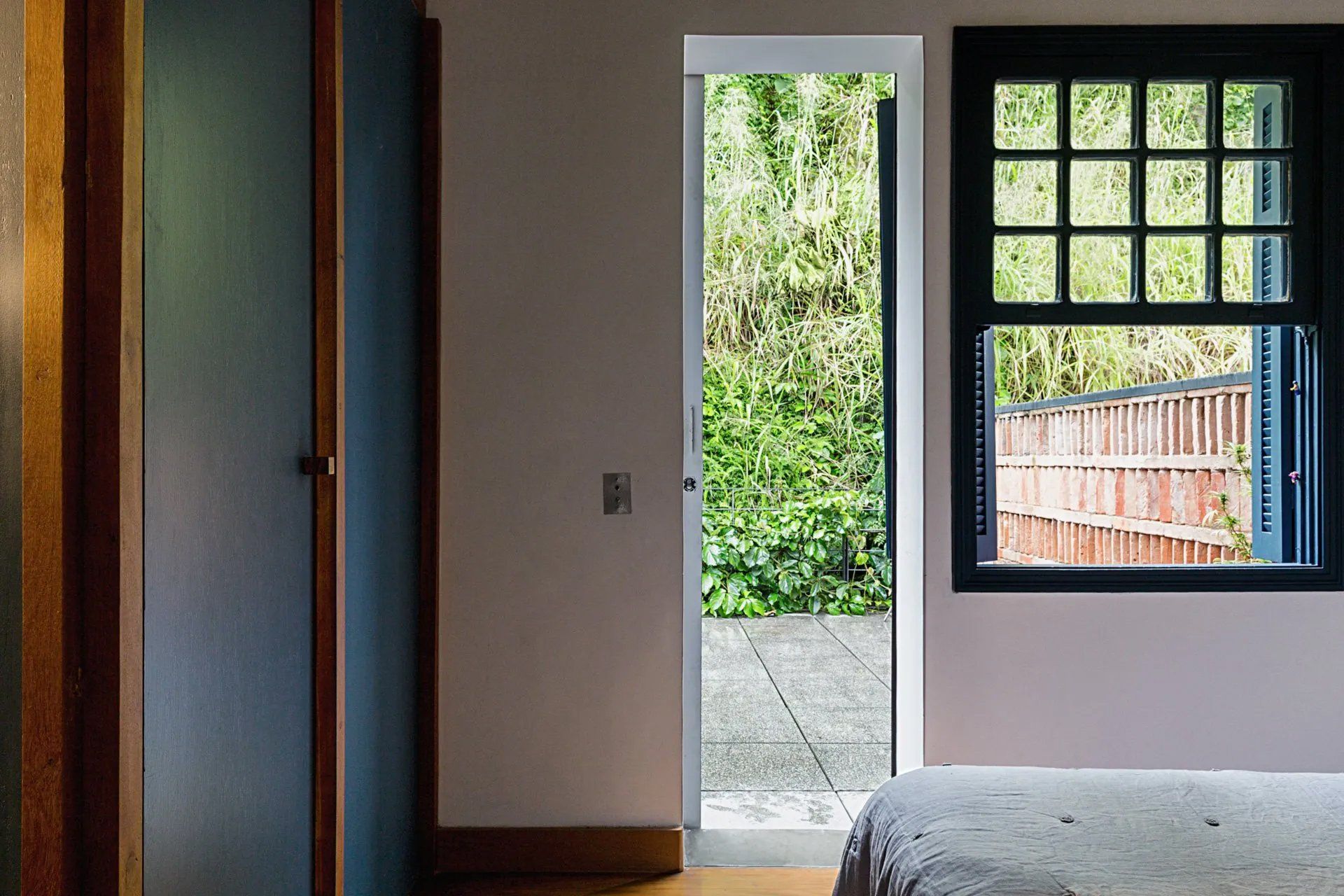 Um quarto com cama, janela e porta que dá para um pátio.