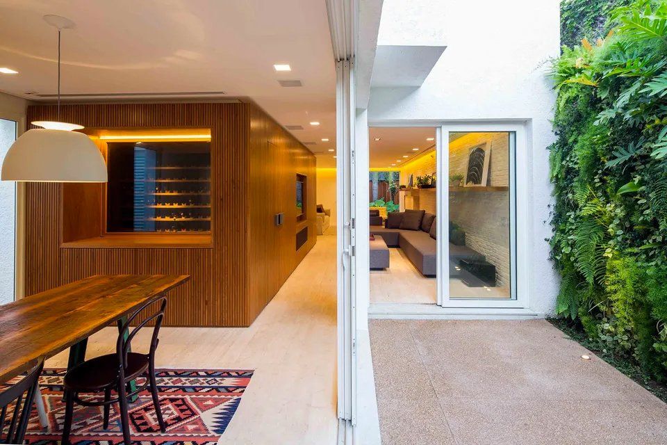 Uma sala de jantar com mesa e cadeiras de madeira e uma porta de correr de vidro que dá acesso a uma sala de estar.