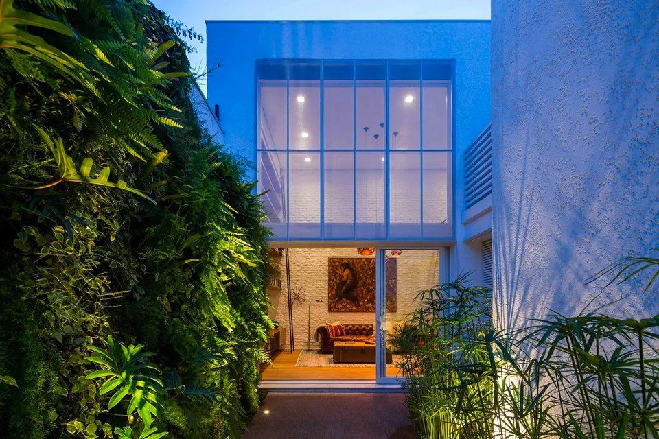 Uma casa com muitas janelas é cercada por árvores e plantas.