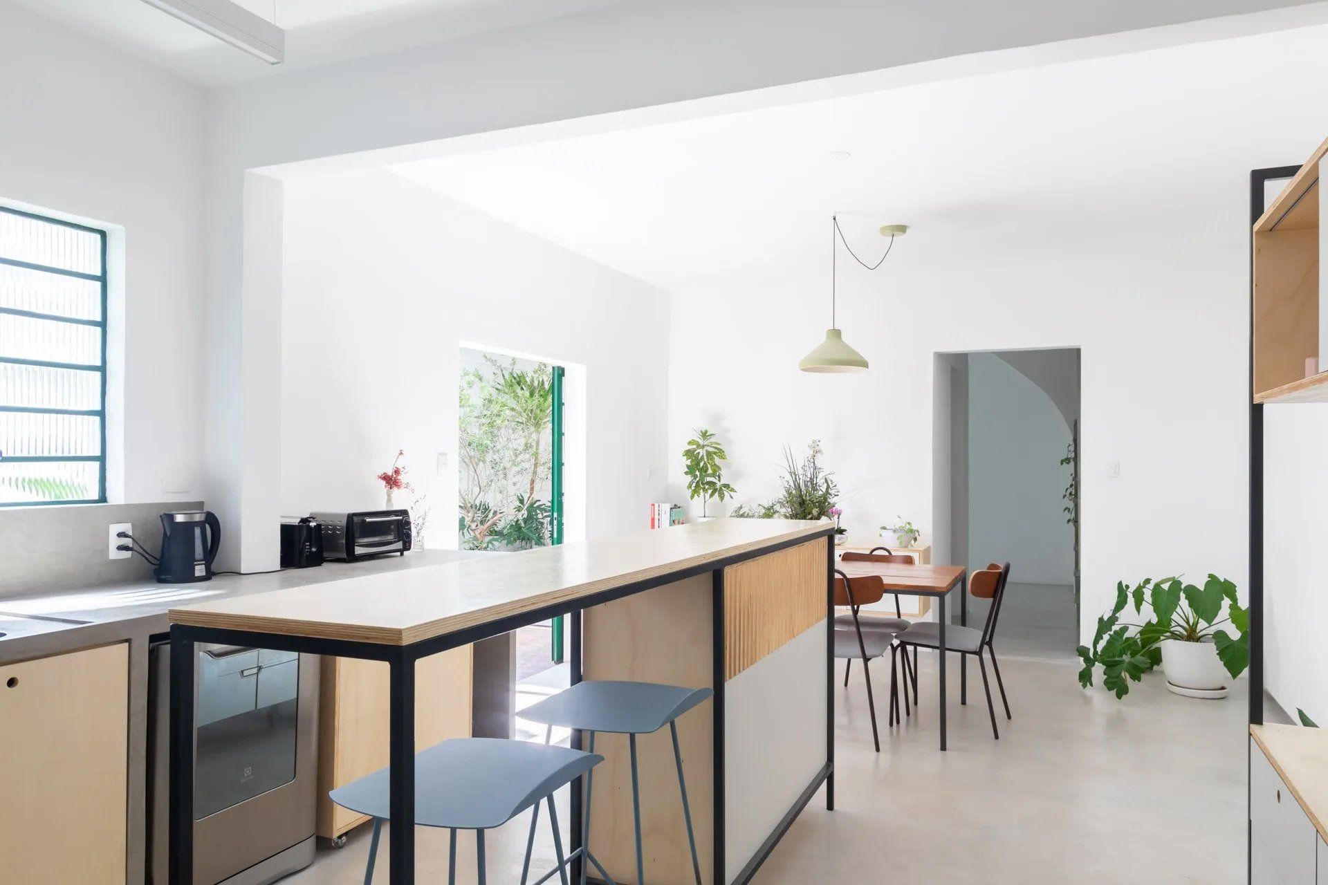 Uma cozinha com um longo balcão e bancos e uma sala de jantar ao fundo.