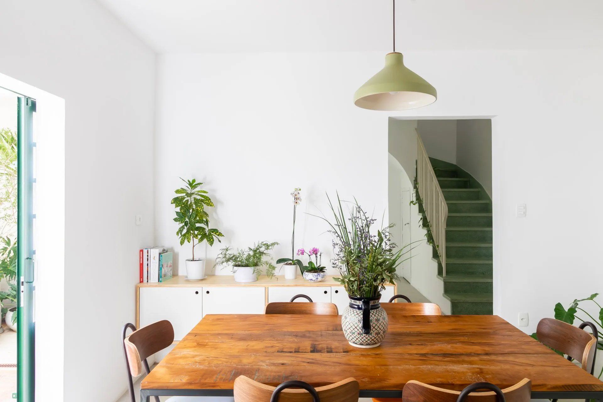 Uma sala de jantar com mesa e cadeiras de madeira e uma escada verde.