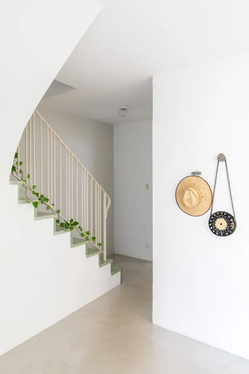 Uma escadaria branca com um chapéu e uma bolsa pendurados na parede.