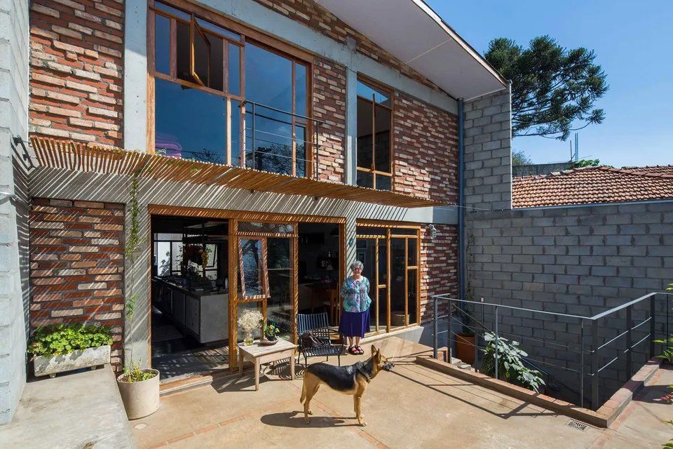 Uma mulher e um cachorro estão parados em frente a uma casa grande.