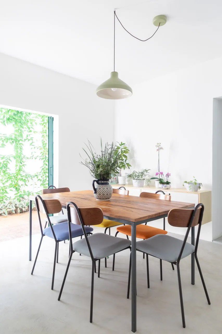 Uma sala de jantar com mesa e cadeiras e um vaso de flores sobre a mesa.