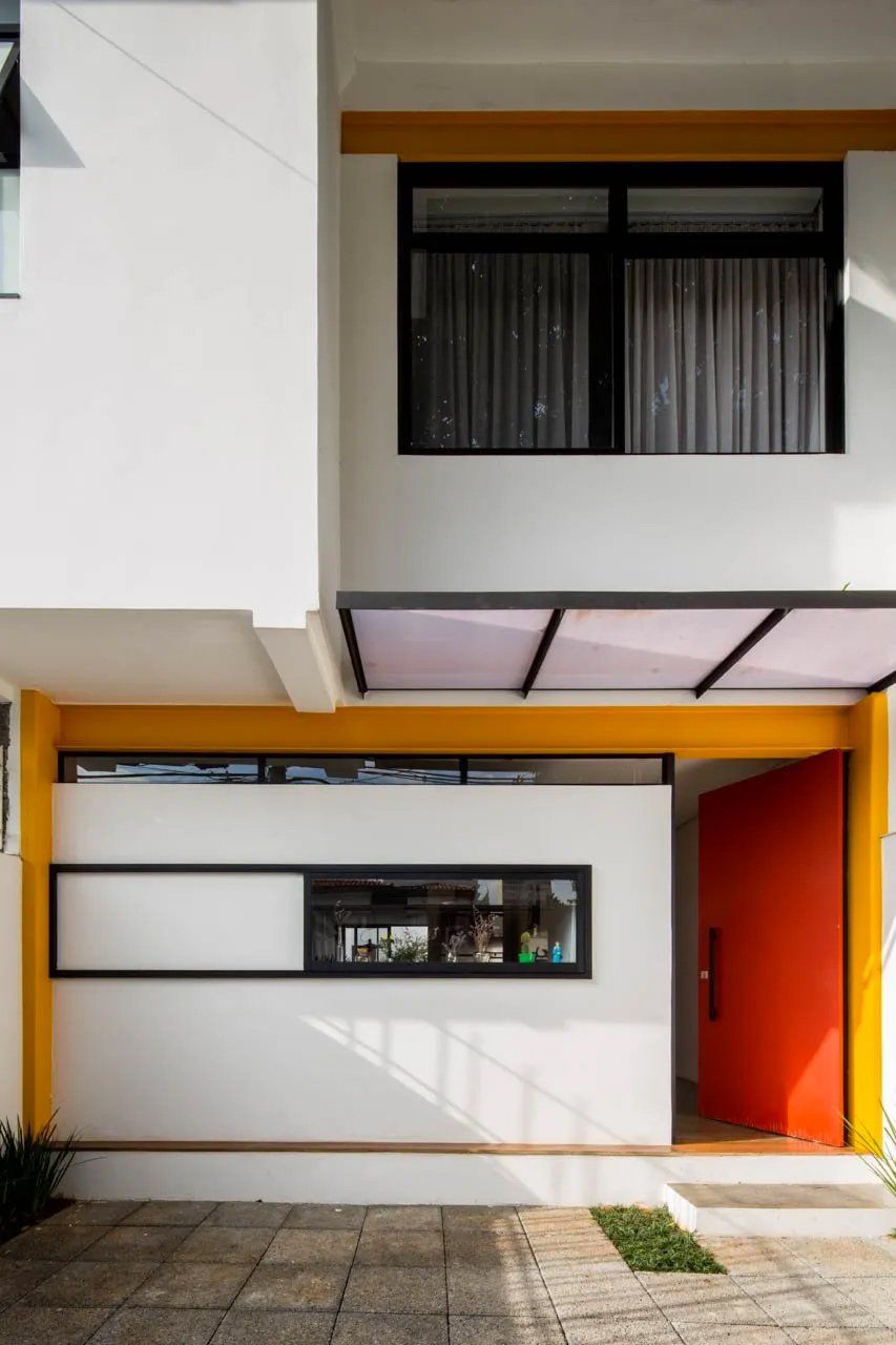 Uma casa branca com porta vermelha e detalhes amarelos