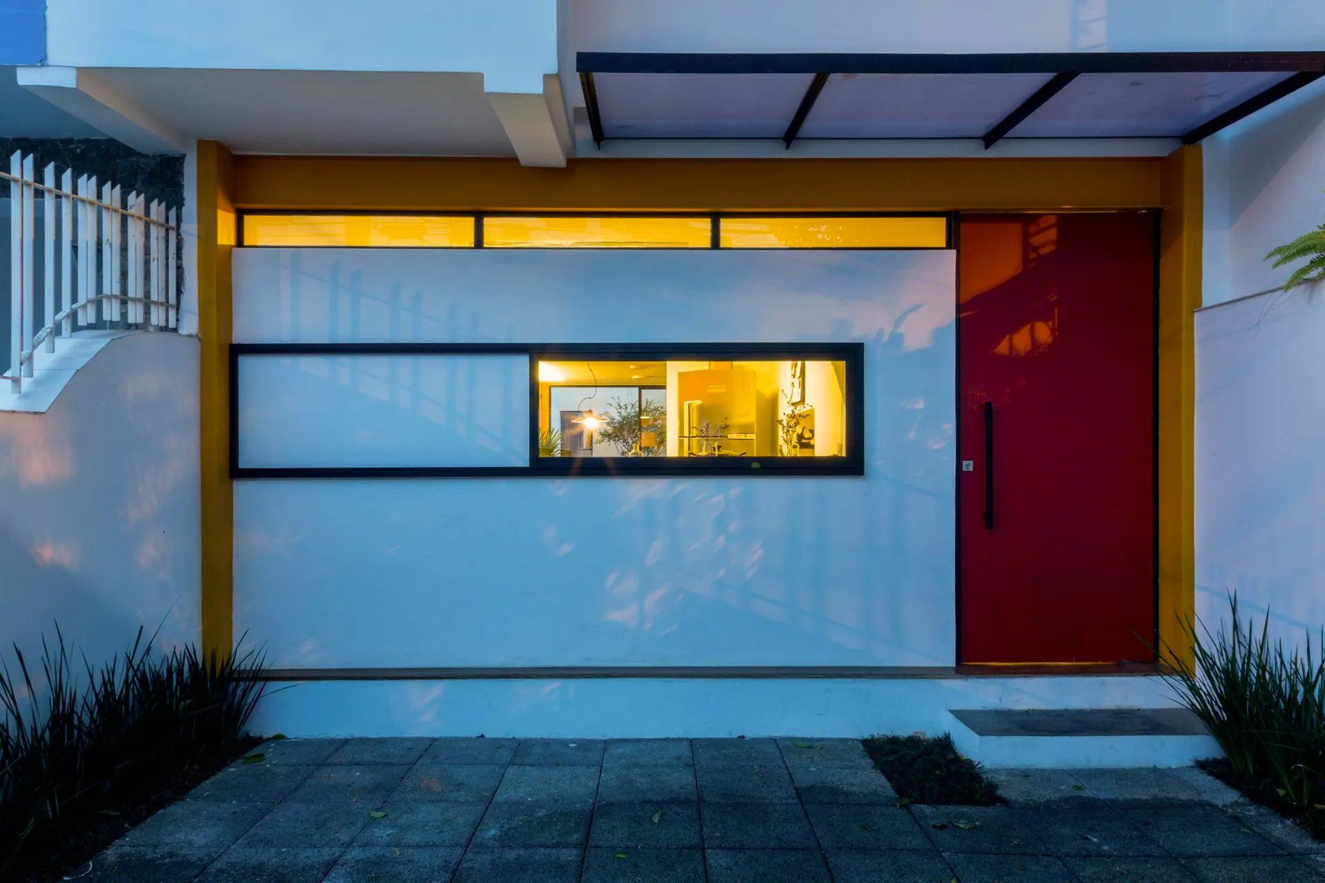 Uma casa branca com porta vermelha e detalhes amarelos