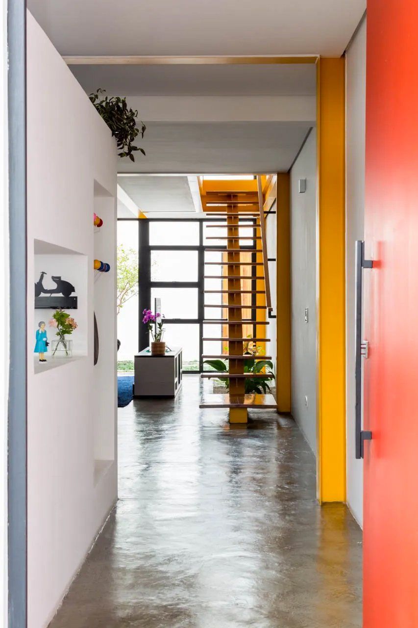 Um corredor em uma casa com uma porta vermelha e uma escada amarela