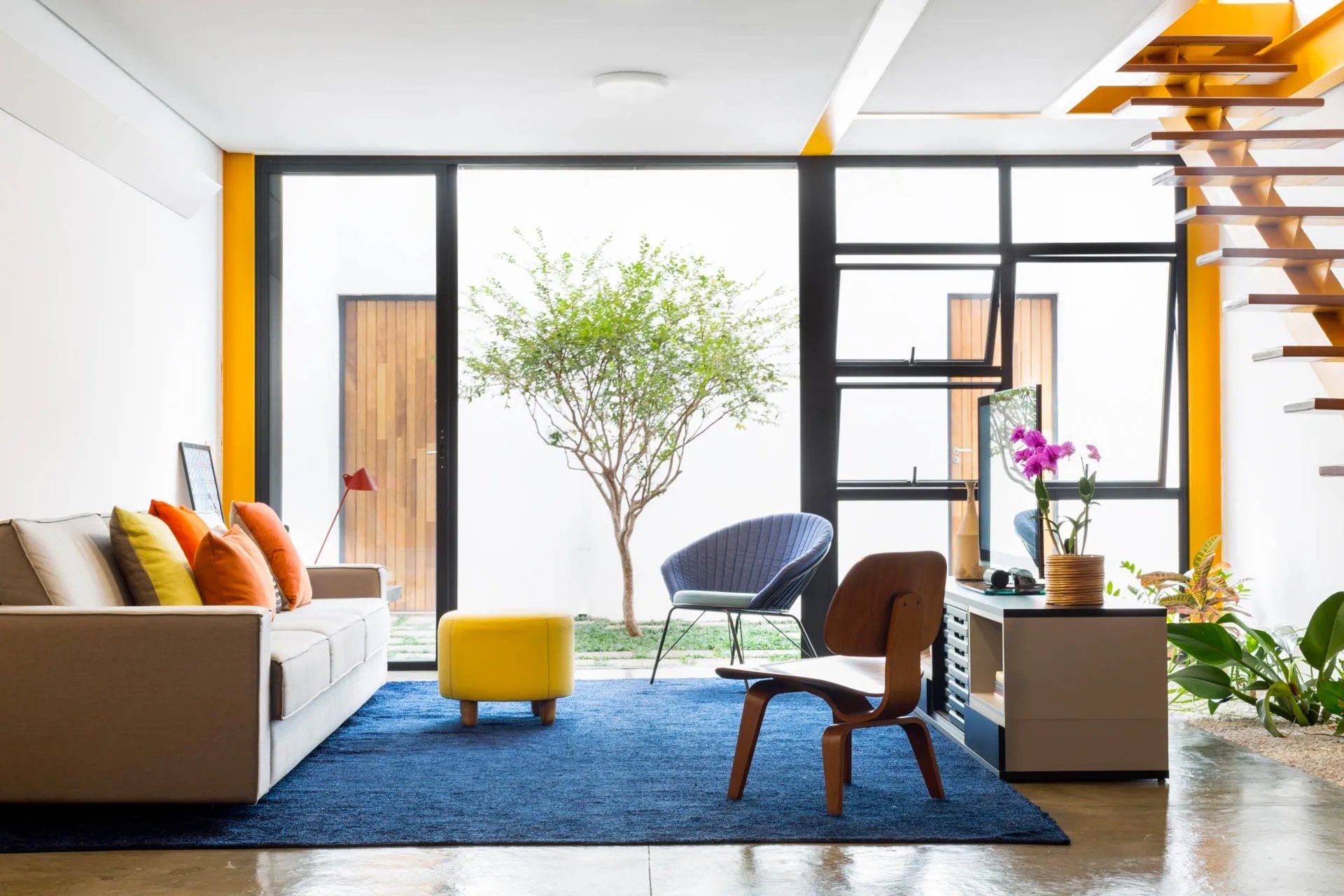 Uma sala com sofá, cadeira, pufe e tapete azul.