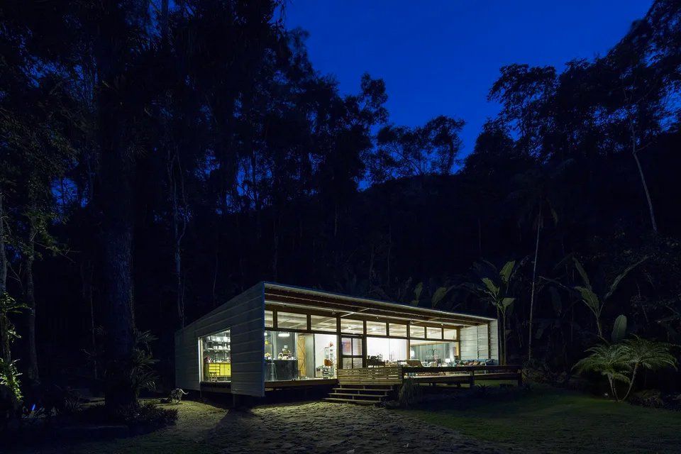 Uma casa está iluminada à noite no meio de uma floresta.
