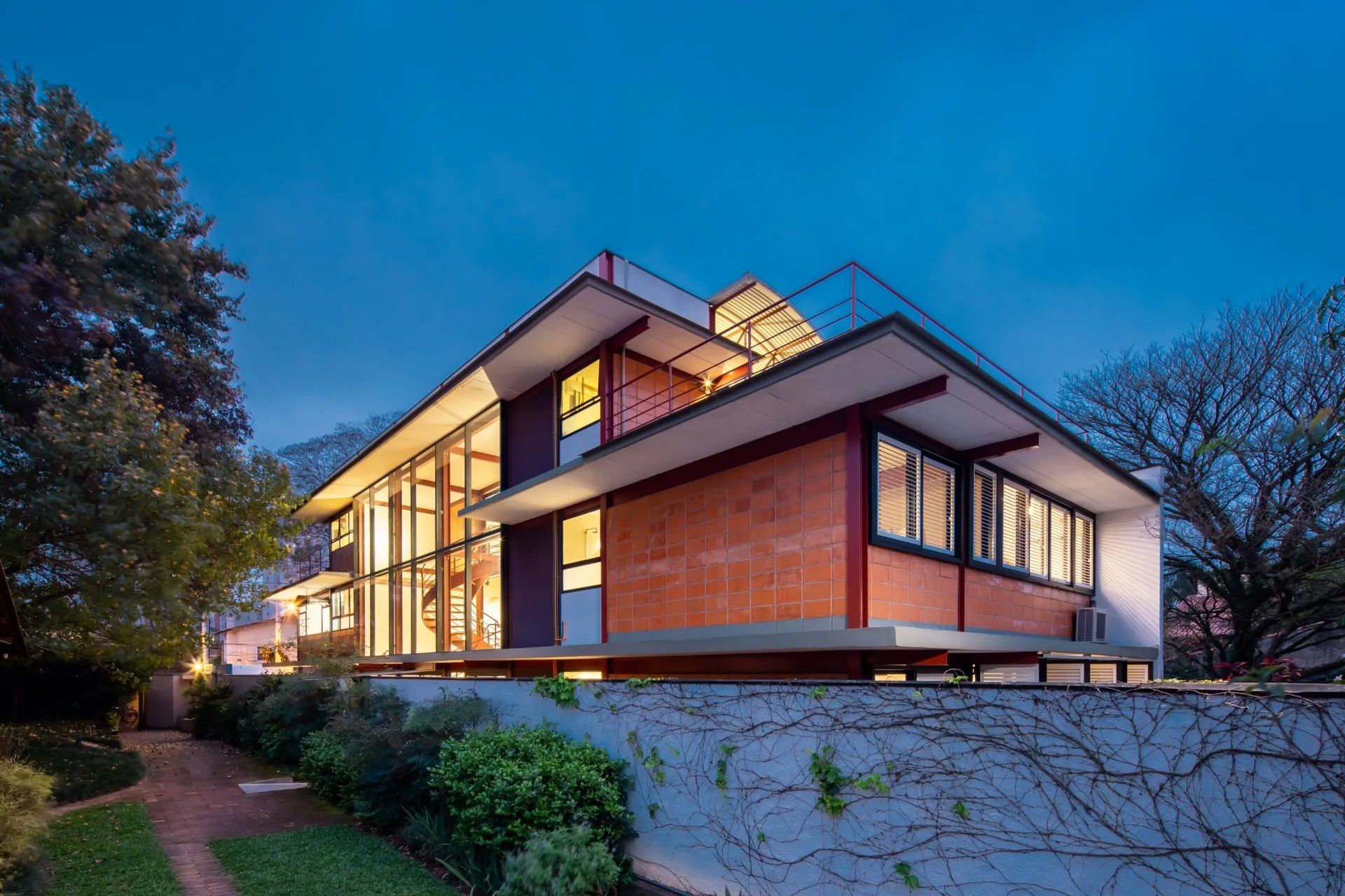 Uma casa grande com muitas janelas fica iluminada à noite.
