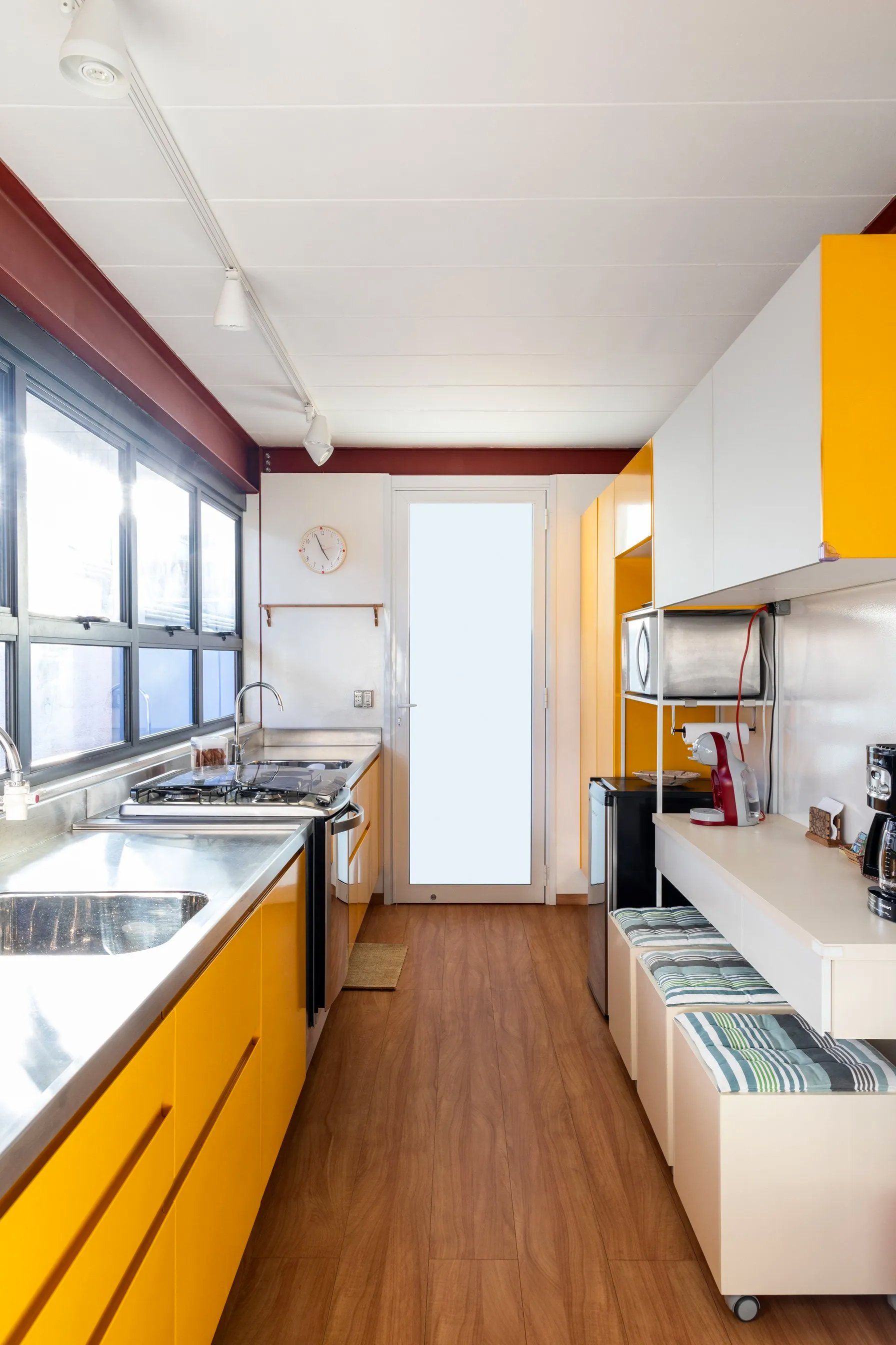 Uma cozinha com armários amarelos, eletrodomésticos de aço inoxidável, pia e uma grande janela.