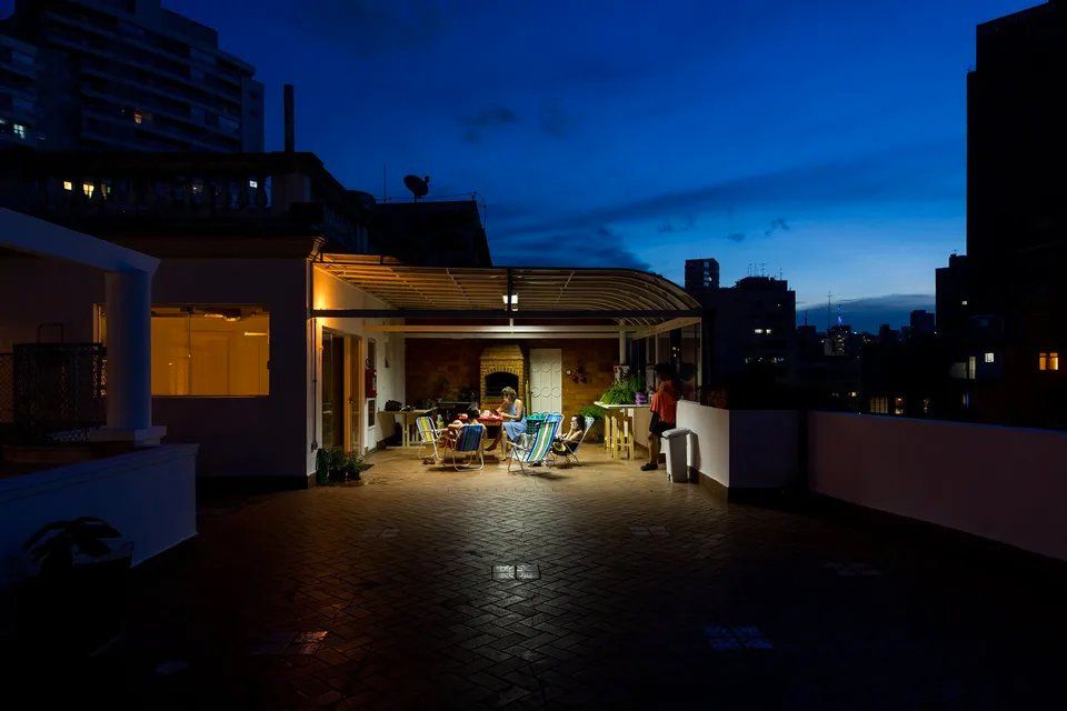 Um grupo de pessoas está sentado em uma mesa no telhado à noite.