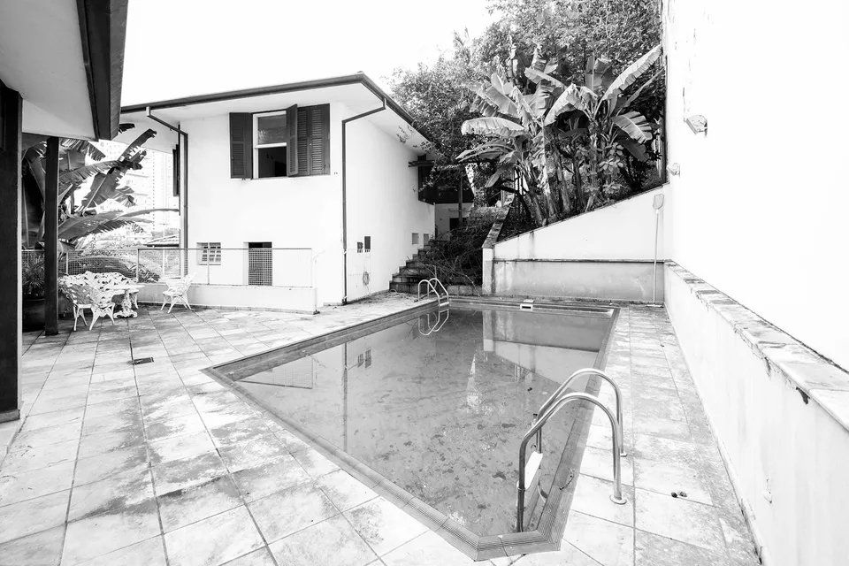 Uma foto em preto e branco de uma piscina em frente a uma casa.