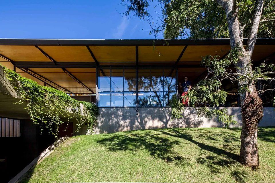 Uma grande casa com muitas janelas está situada no topo de uma colina gramada.