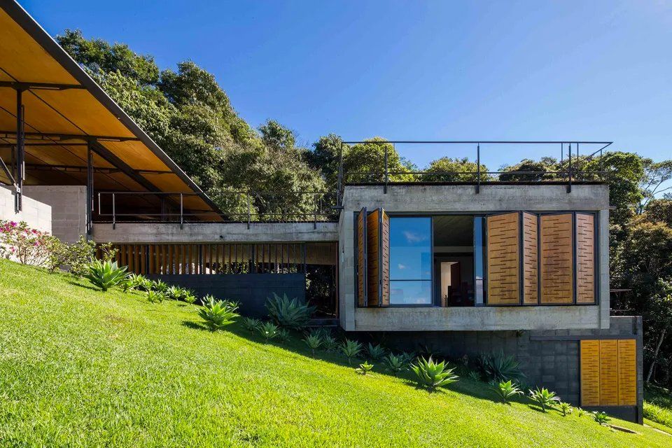 Uma casa moderna está situada no topo de uma colina gramada cercada por árvores.