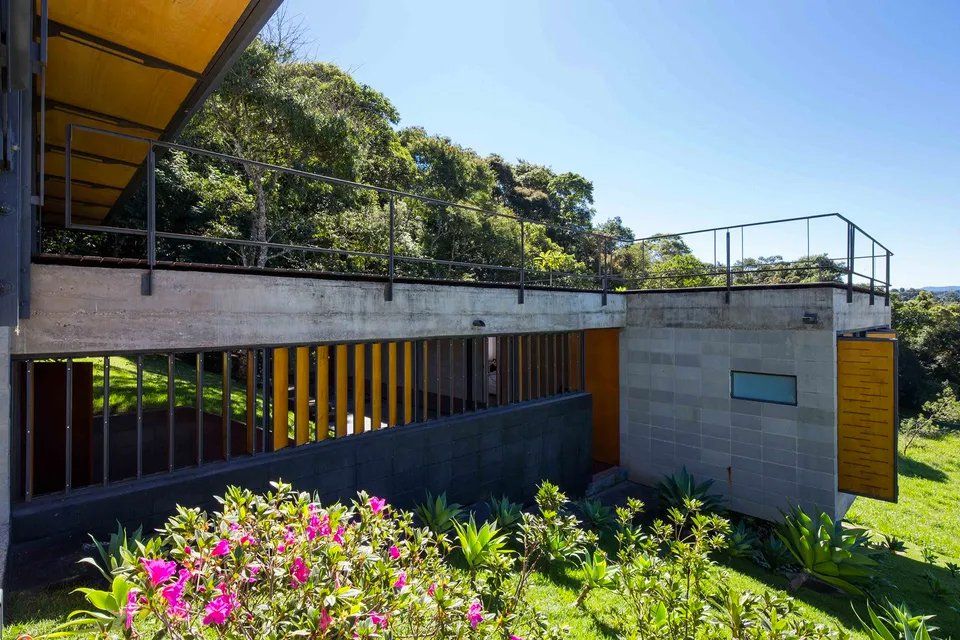 Uma casa moderna com telhado verde é cercada por árvores e flores.