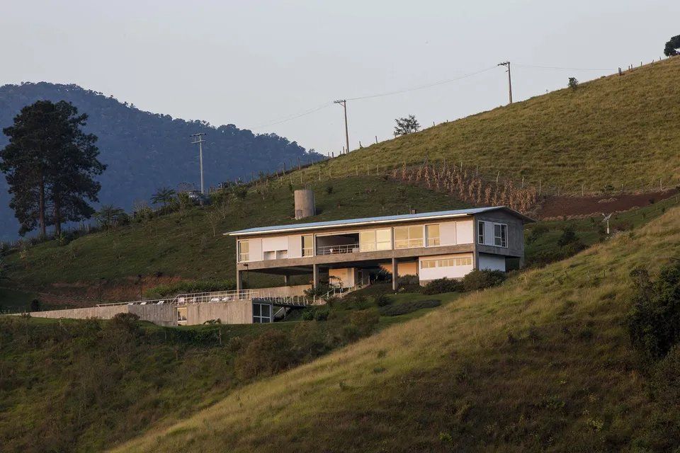 Uma casa no topo de uma colina gramada com montanhas ao fundo
