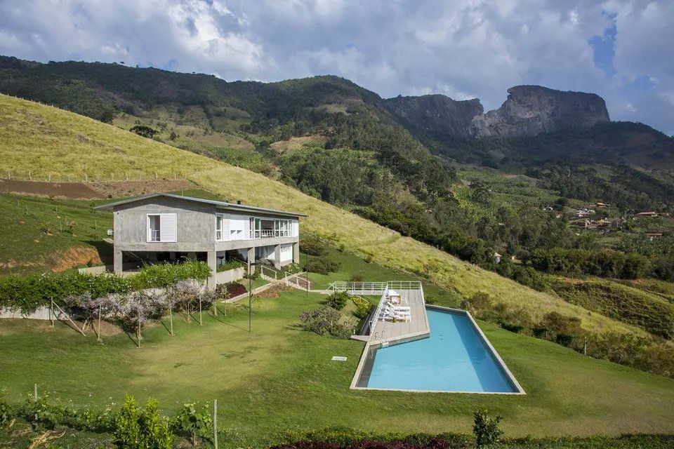 Uma casa com piscina no meio de um campo verdejante rodeado de montanhas.
