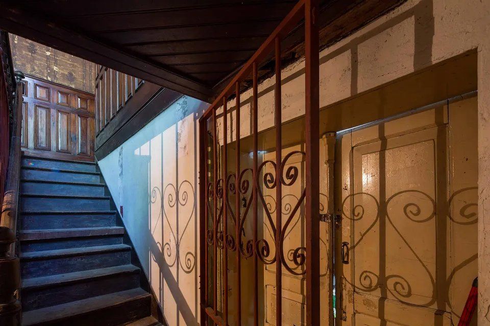 Uma escada com corrimão de ferro forjado e uma sombra na parede.