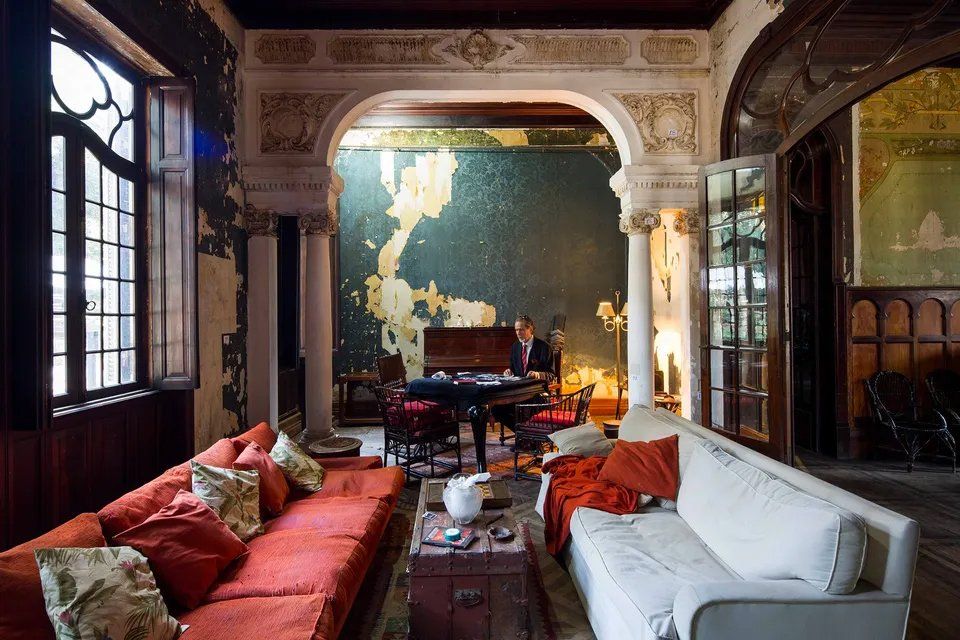 Um homem toca piano em uma sala cheia de móveis.