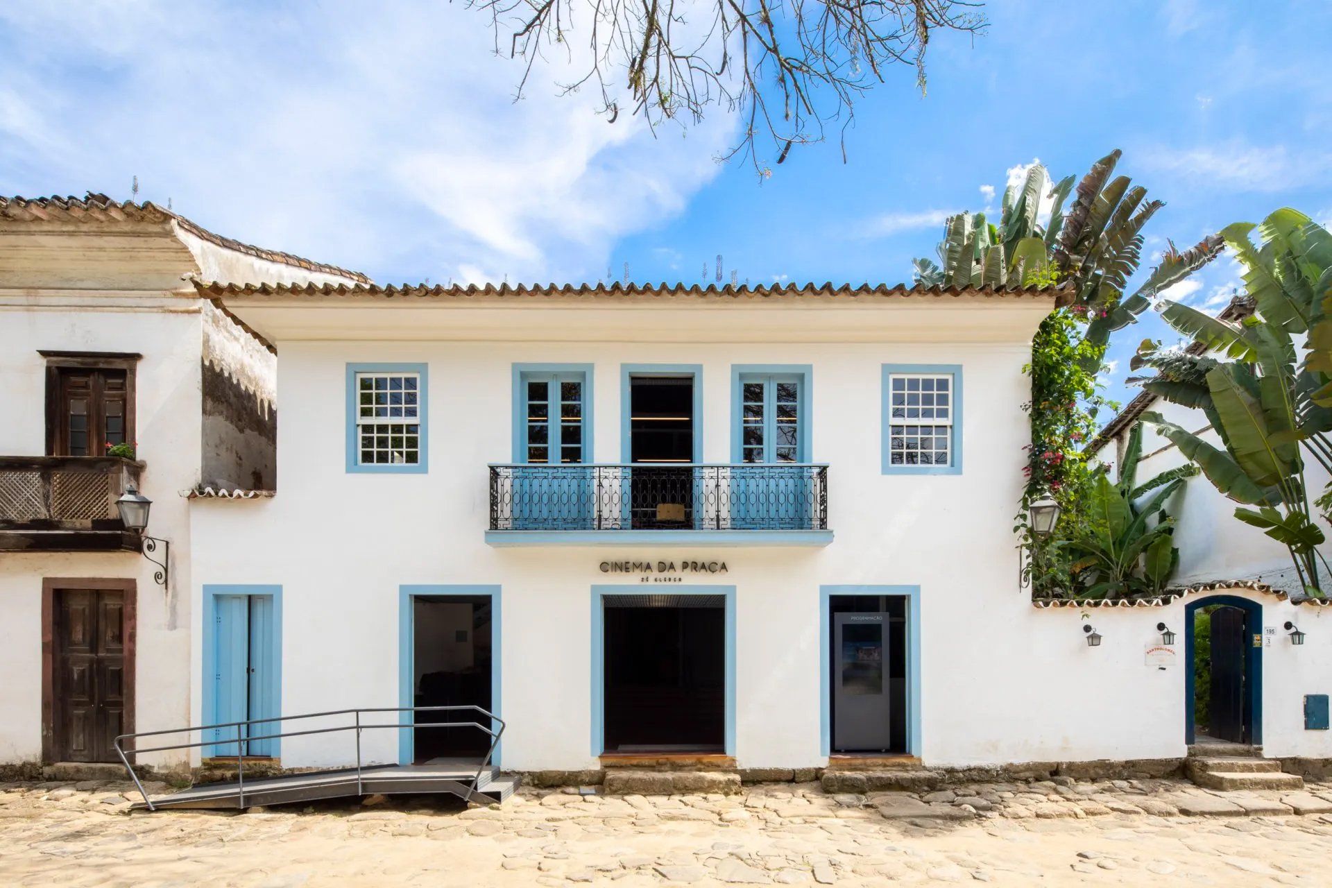 Um prédio branco com uma varanda azul e uma rampa para cadeiras de rodas na frente.