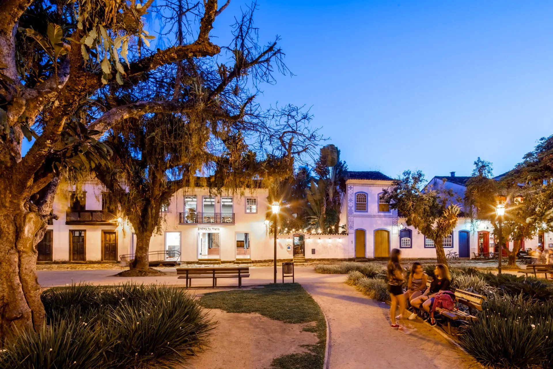 Algumas pessoas estão sentadas em um banco de um parque à noite.