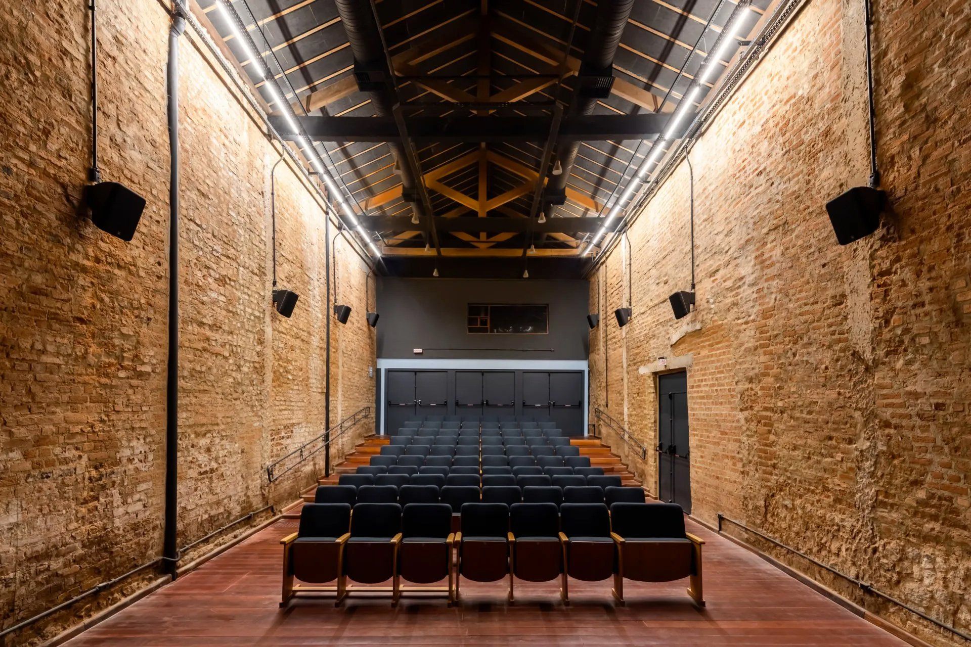 Um auditório vazio com parede de tijolos e poltronas de madeira.