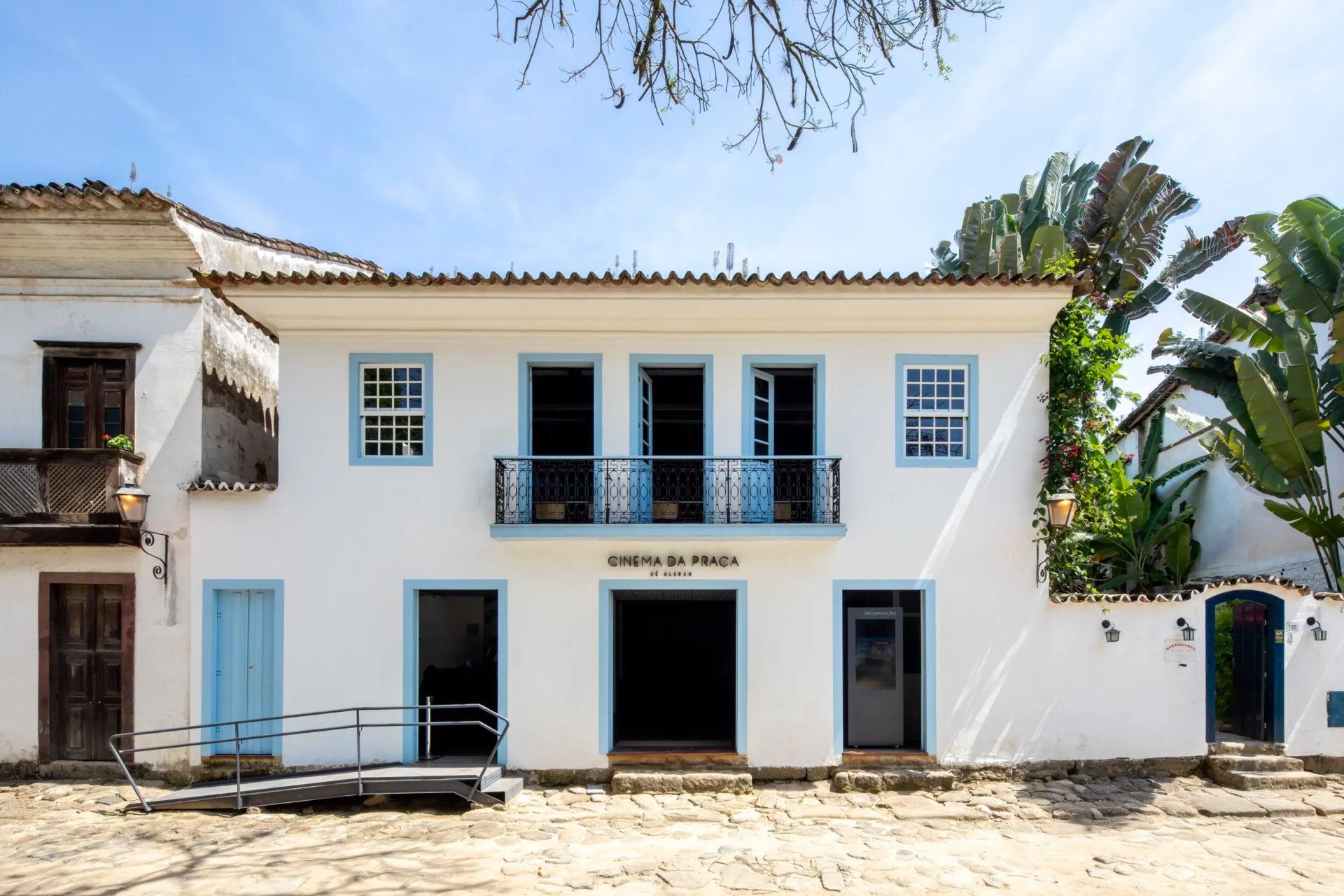 Um prédio branco com detalhes em azul e uma rampa para cadeiras de rodas na frente.