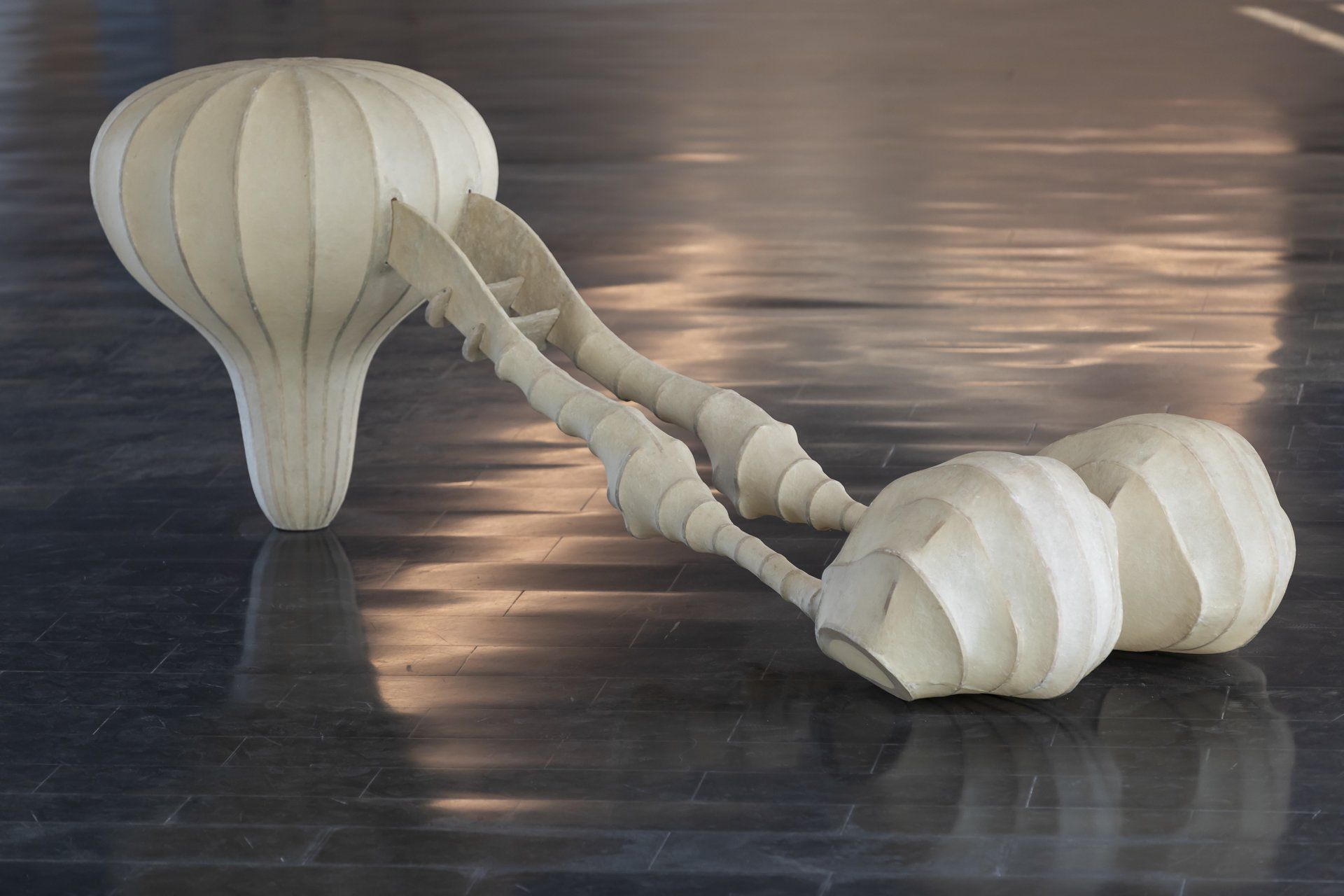 Duas esculturas brancas estão sobre um chão de madeira