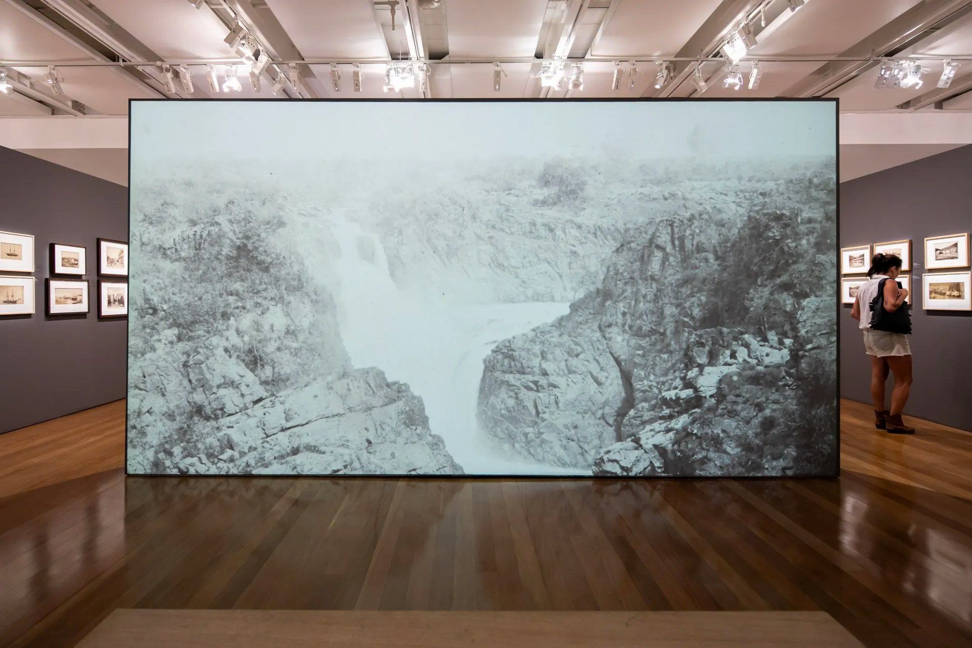 Duas pessoas estão olhando para uma grande foto de uma cachoeira em um museu.