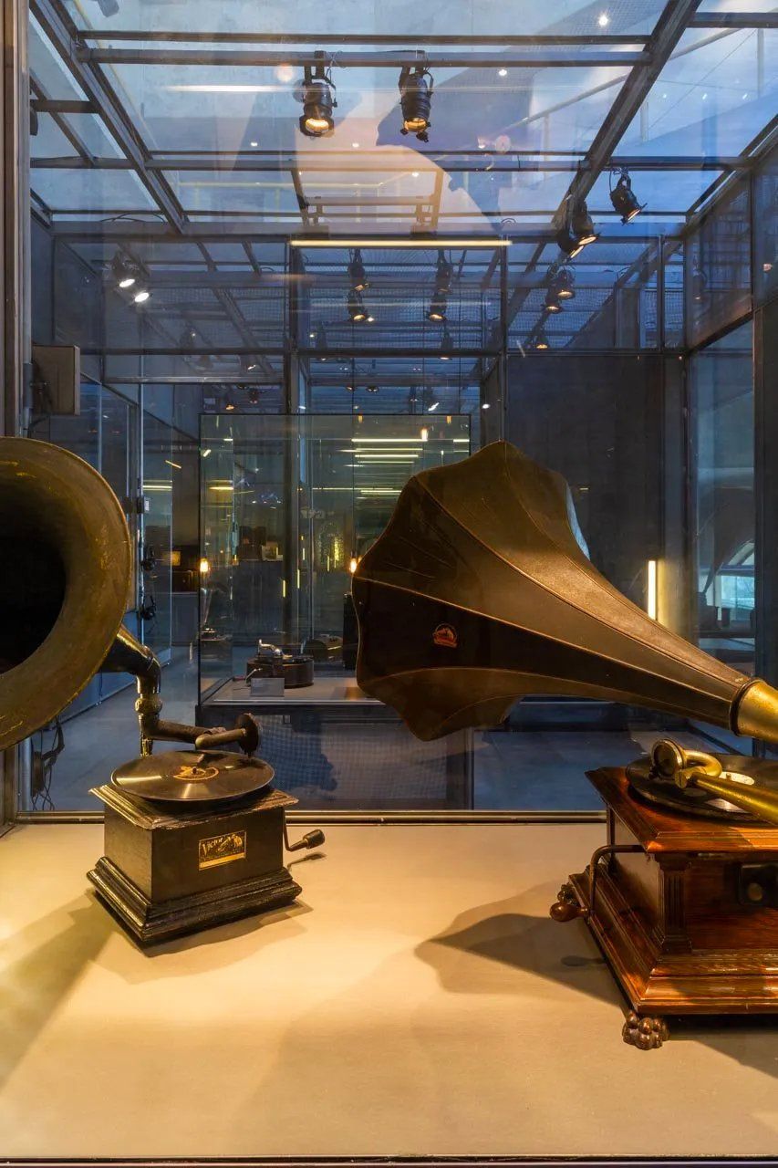 Dois fonógrafos estão sobre uma mesa em uma caixa de vidro.