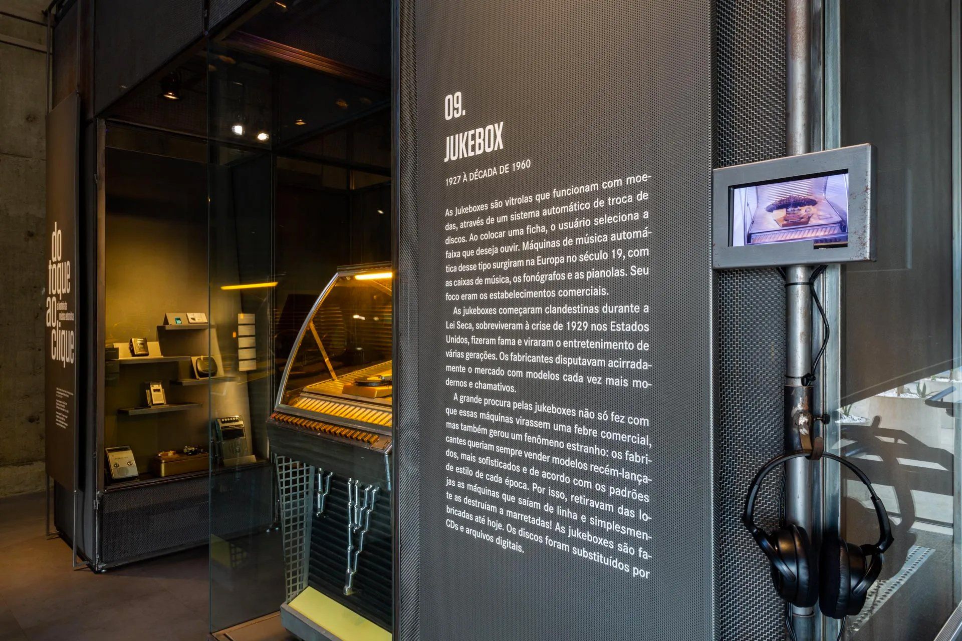 Uma sala com vitrine, placa, fones de ouvido e monitor.