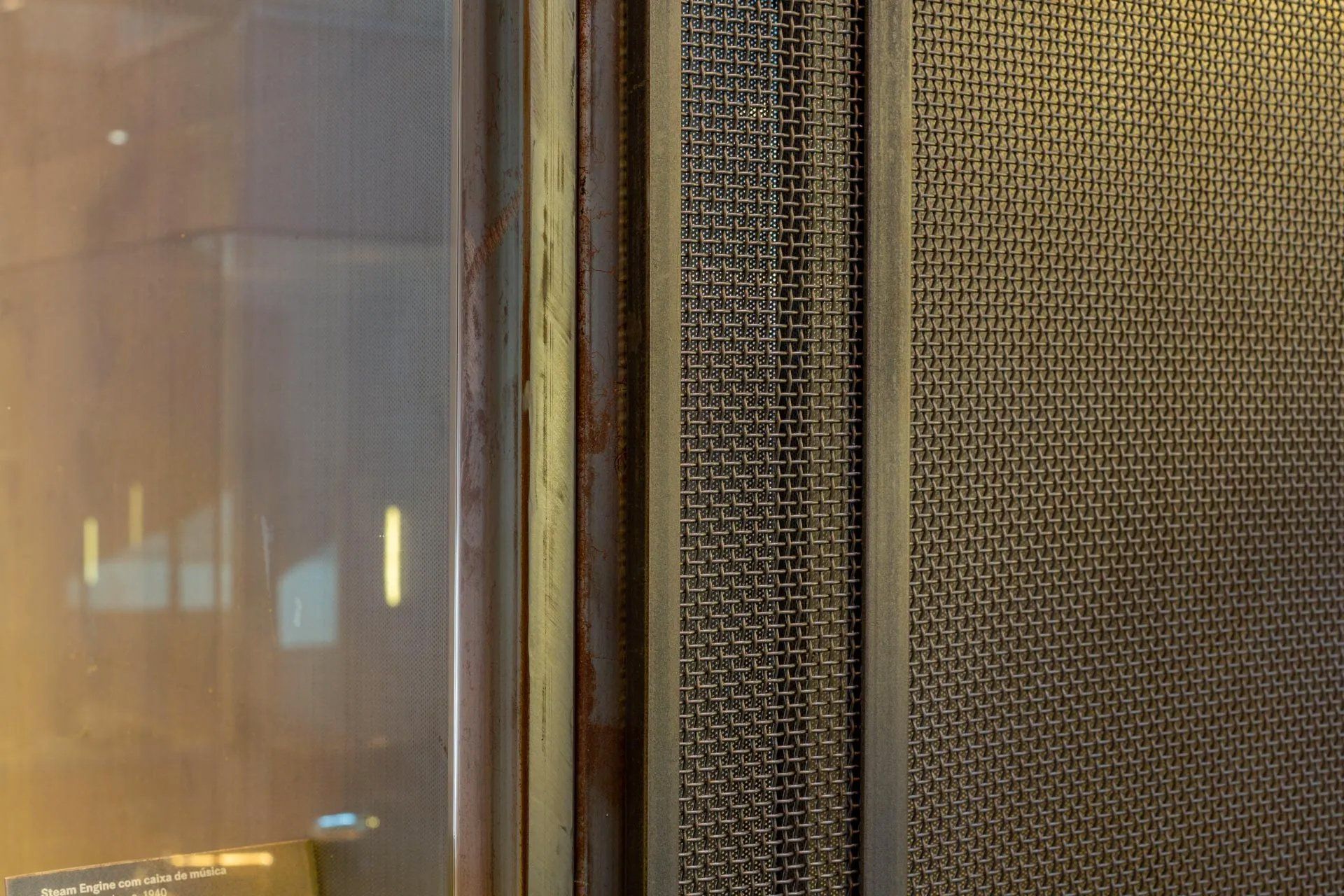 Um close de uma parede de metal com uma janela ao fundo.