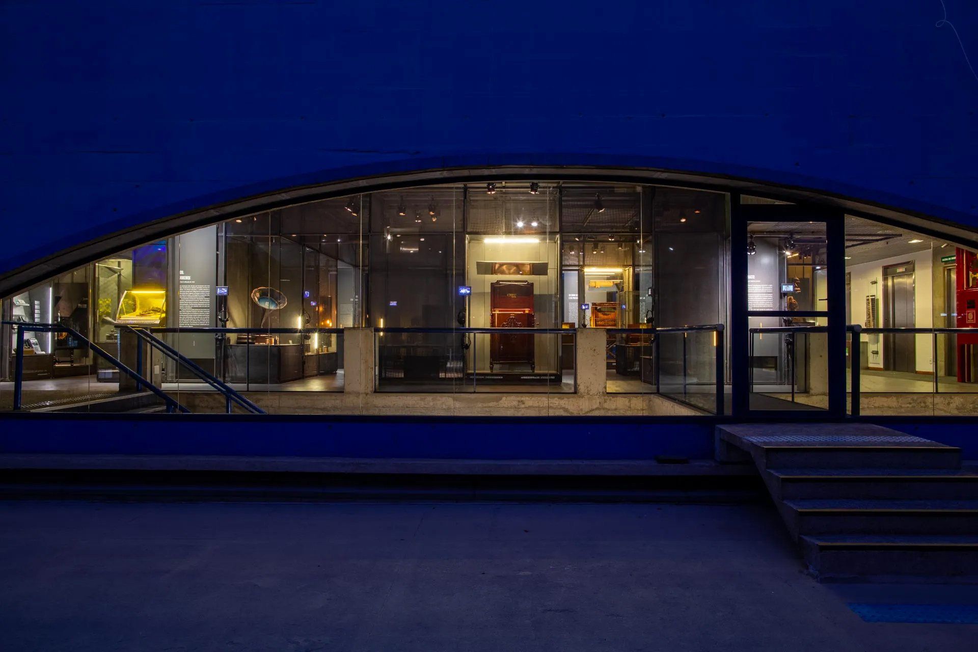 Um prédio azul com uma grande janela e escadas que levam até ele à noite.