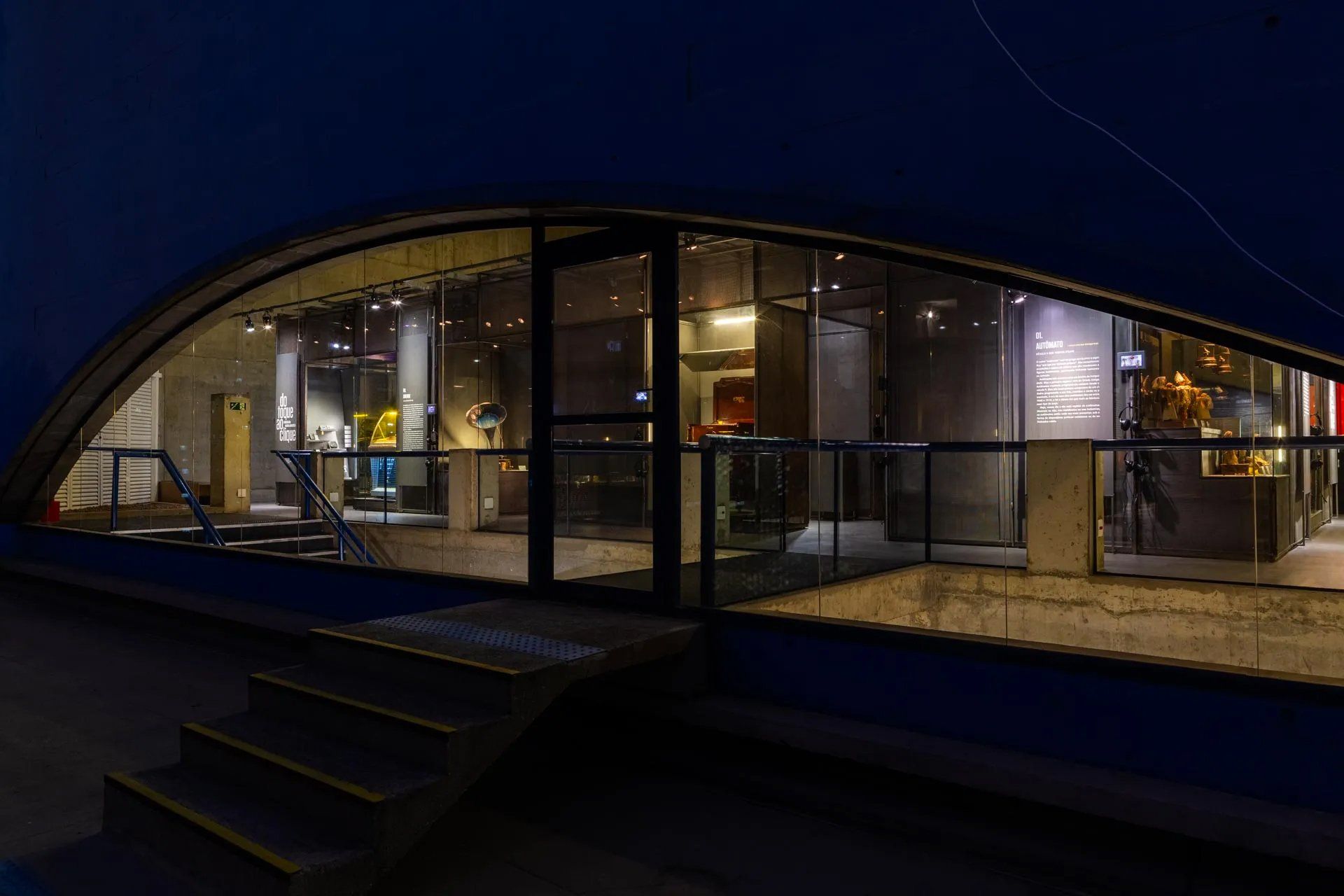 Um grande edifício de vidro com escadas que levam até ele à noite.