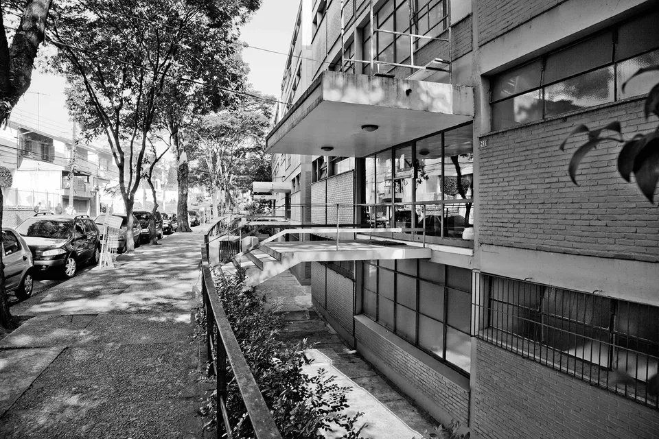 Uma foto em preto e branco de um prédio com carros estacionados em frente.