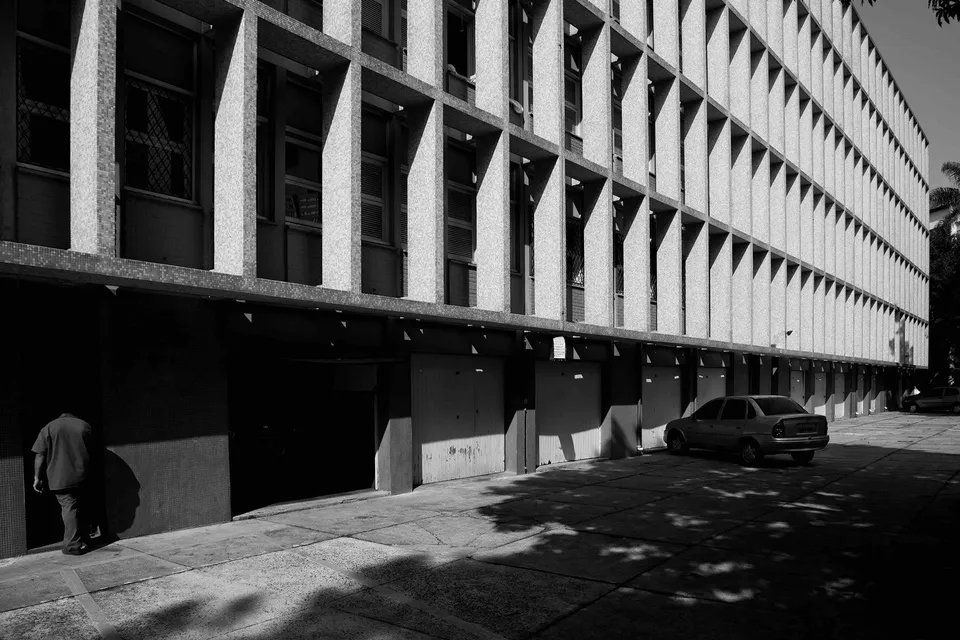 Uma foto em preto e branco de um prédio com um carro estacionado em frente.