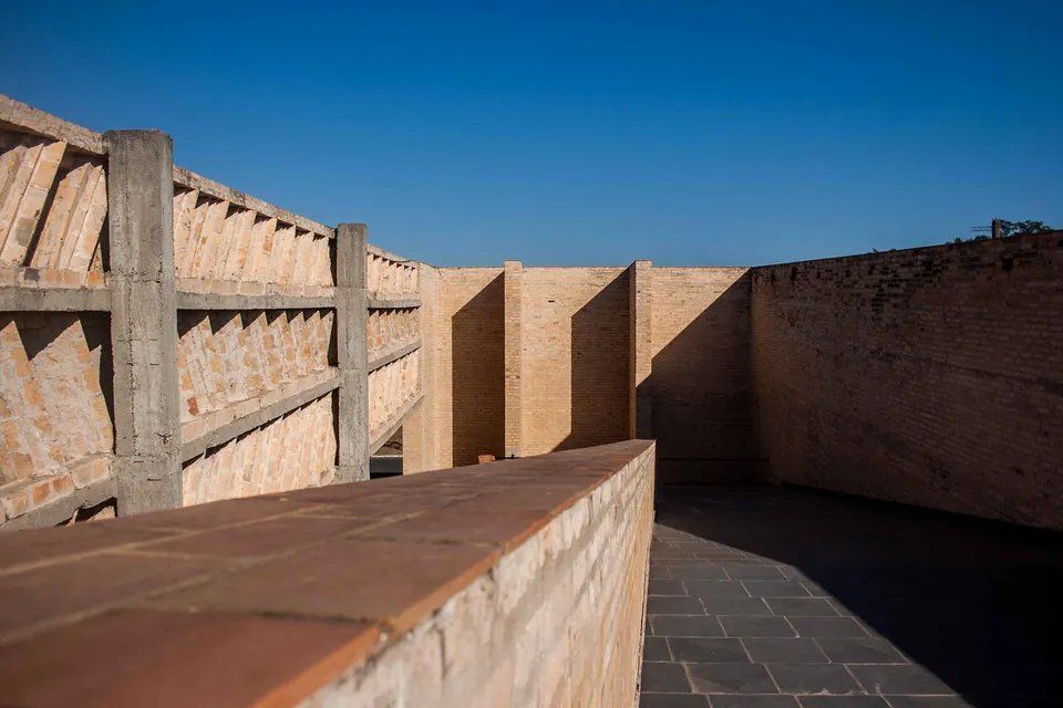 Uma parede de tijolos com uma cerca ao fundo e um céu azul ao fundo.