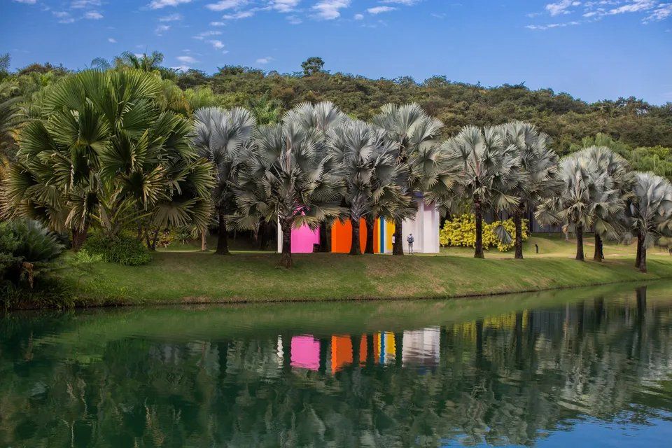 Uma fileira de tendas coloridas está ao lado de um lago cercado por árvores.