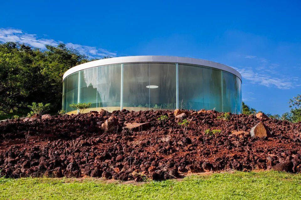 Um edifício redondo de vidro está situado no topo de uma colina rochosa.