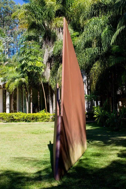 Uma grande escultura está no meio de um parque verdejante.