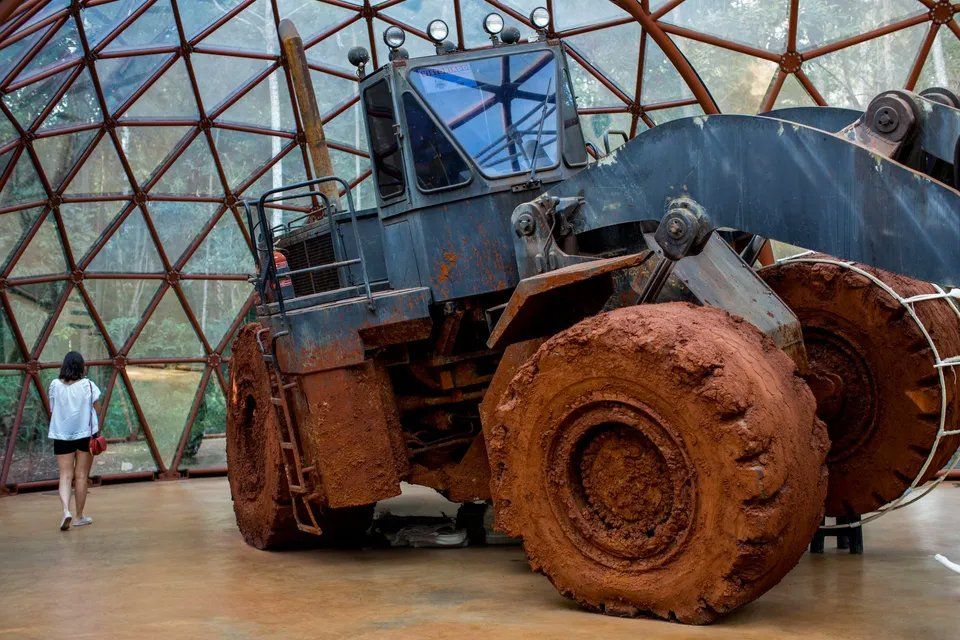 Uma mulher está diante de um grande trator em uma cúpula.