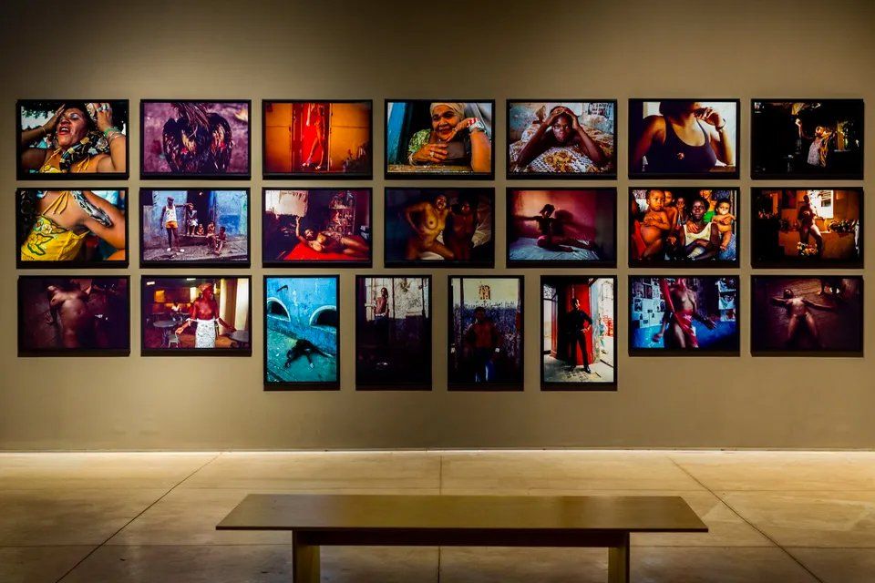 Uma parede com muitas fotos e um banco em primeiro plano.