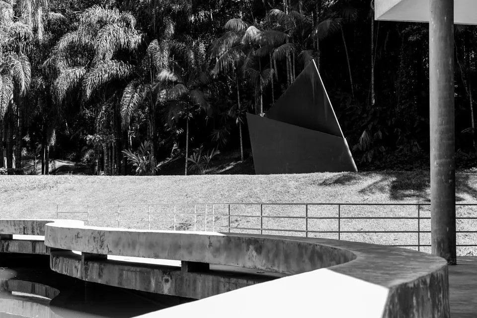 Uma foto em preto e branco de uma ponte em um parque com árvores ao fundo.