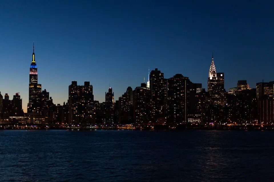 Uma silhueta do horizonte de uma cidade à noite com um corpo de água em primeiro plano.