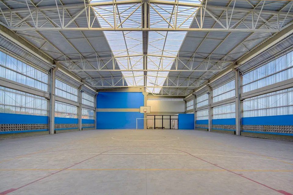 Um grande armazém vazio com muitas janelas e uma quadra de basquete.