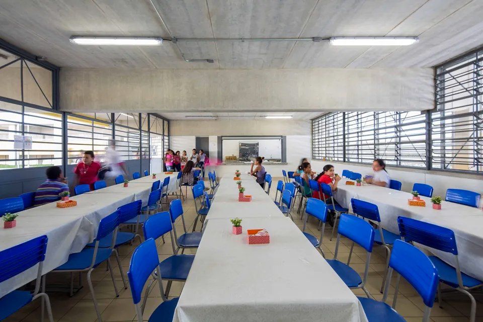Um grupo de pessoas está sentado em mesas compridas em uma sala de jantar.