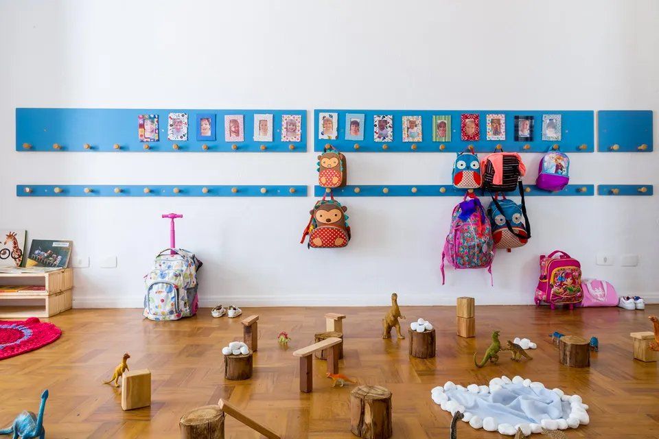 Uma sala com mochilas penduradas na parede e brinquedos no chão.