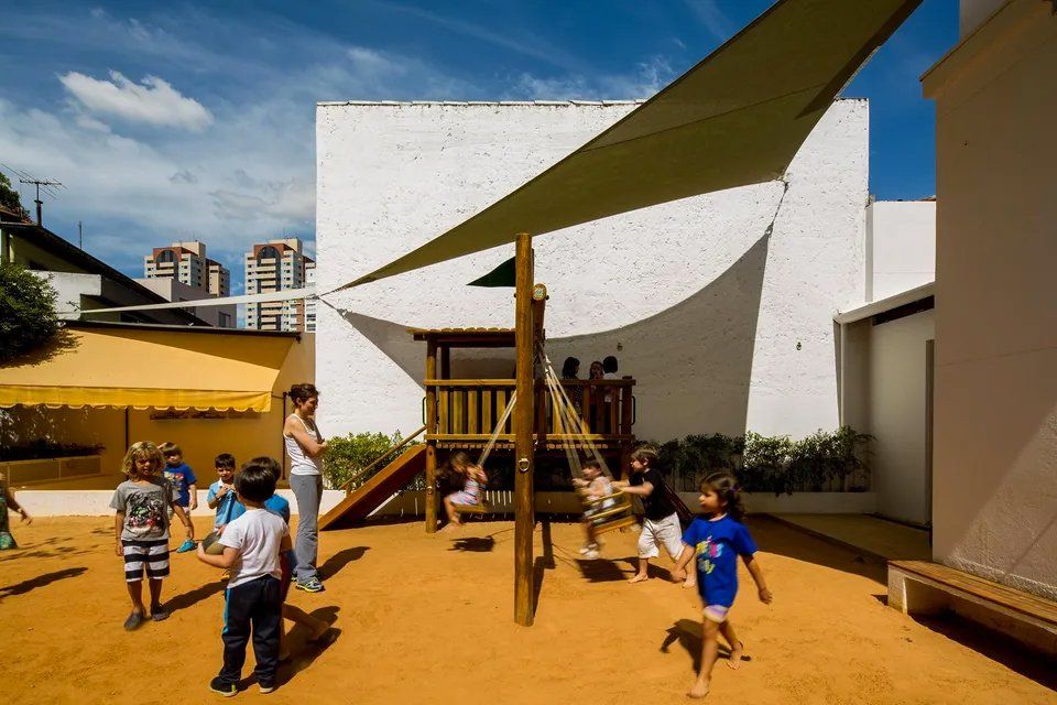 Um grupo de crianças está brincando em um playground sob um guarda-chuva