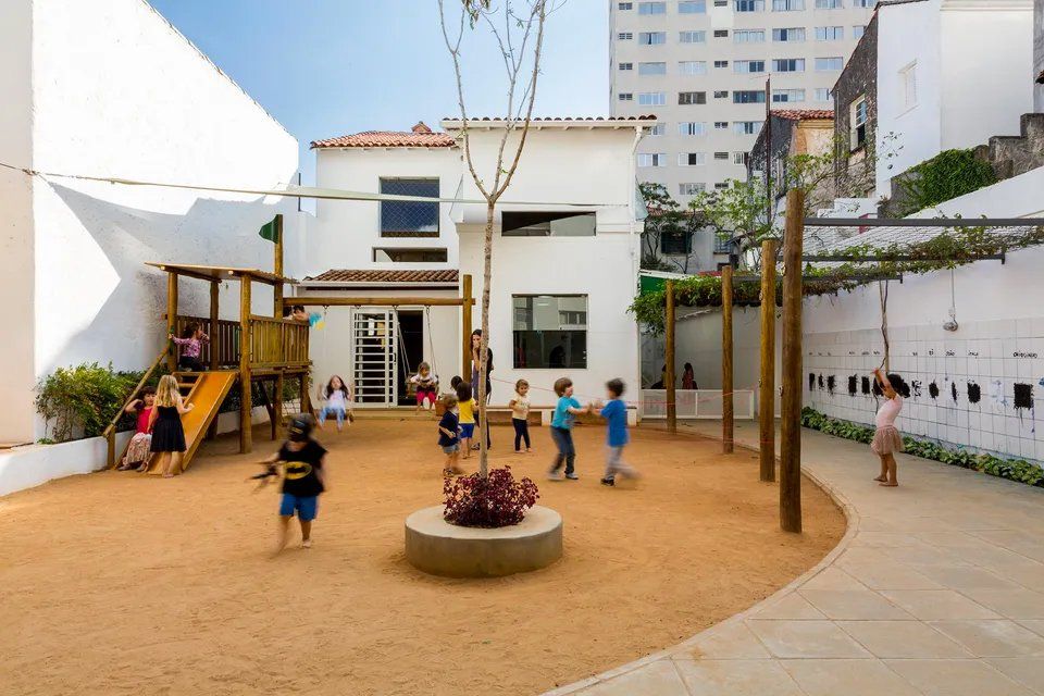 Um grupo de crianças brinca em um playground em frente a um prédio.